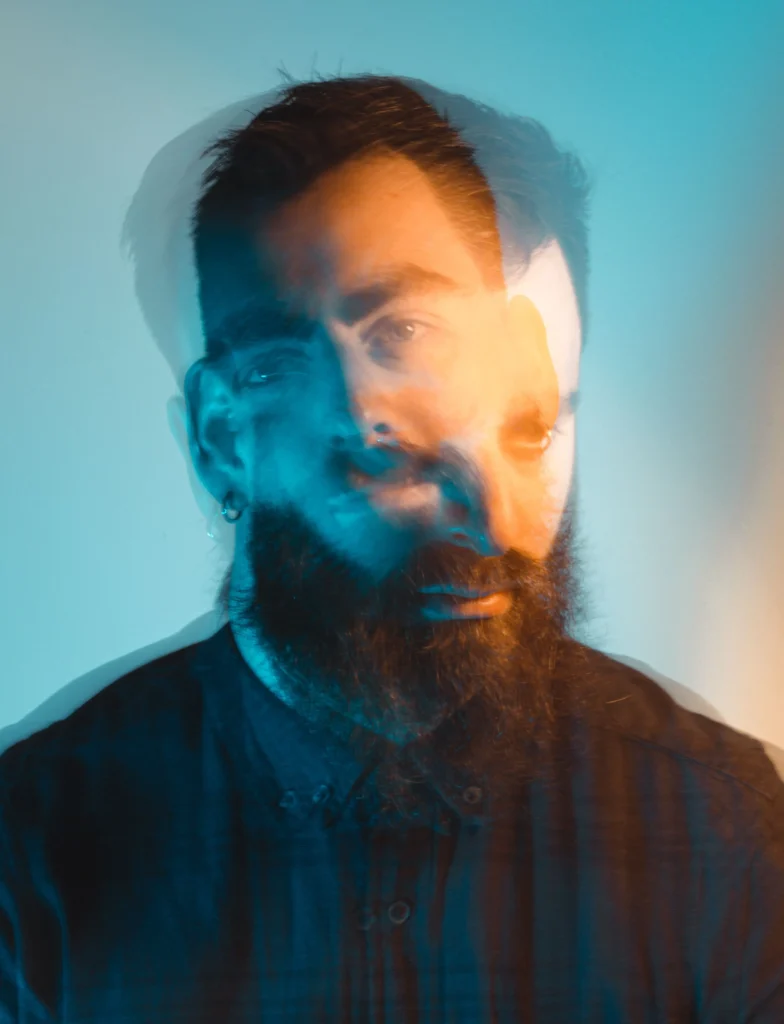An example of a creative headshot showing a dark-haired man with a beard and earring captured in double exposure with vivid colors