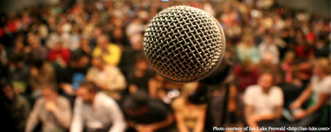 Photo of a microphone, close-up, with a large audience in the blurry background